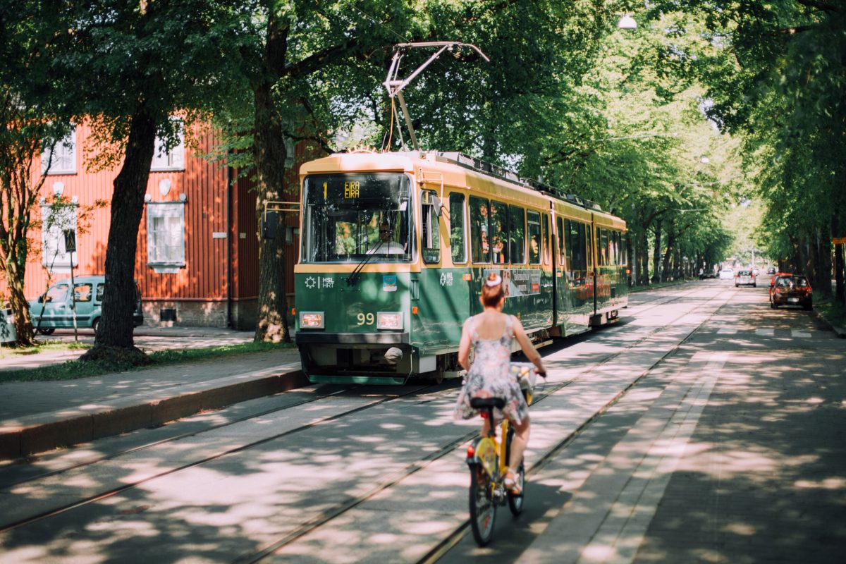 Nainen pyöräilemässä, raitiovaunu taustalla.