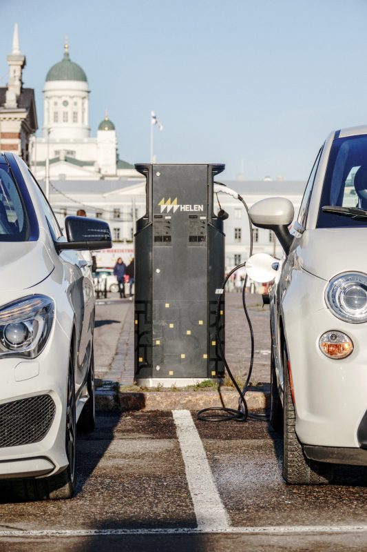 Kaksi sähköautoa latautumassa, taustalla Helsingin tuomiokirkko