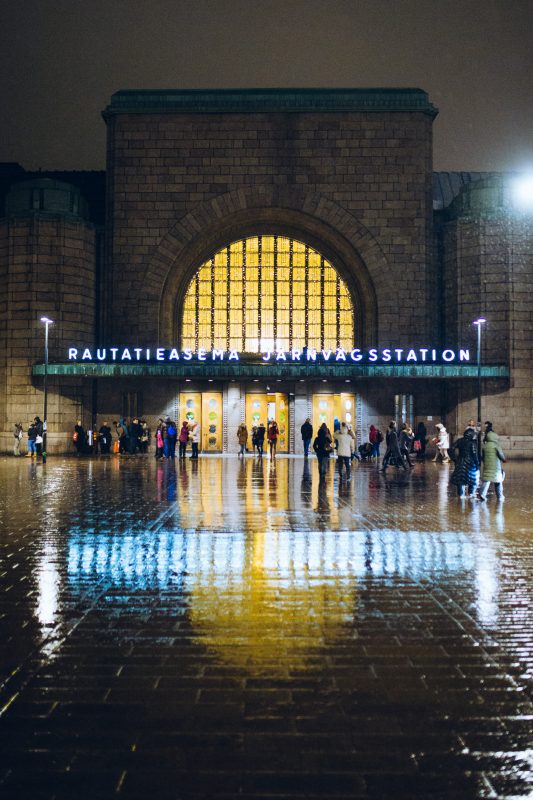 Helsingin rautatieasema illalla vesisateessa, ihmisiä pääovella.