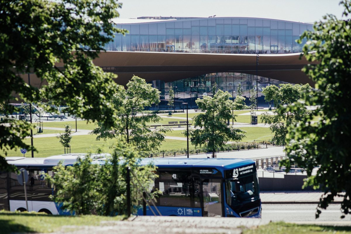 Sininen HSL-bussi etualalla, taustalla puisto ja keskuskirjasto Oodi.